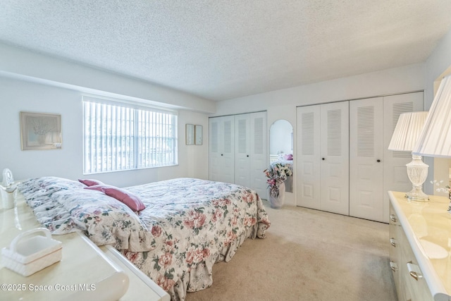 bedroom featuring two closets, light carpet, and a textured ceiling