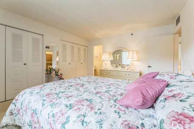 carpeted bedroom featuring arched walkways, visible vents, a textured ceiling, and two closets