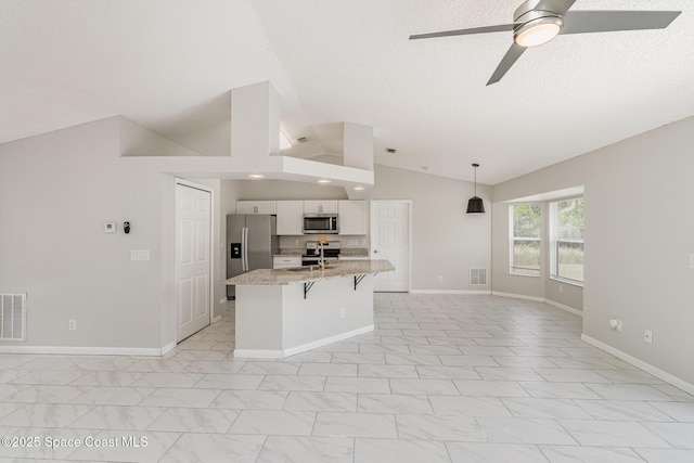 kitchen featuring stainless steel appliances, vaulted ceiling, visible vents, ceiling fan, and a breakfast bar area