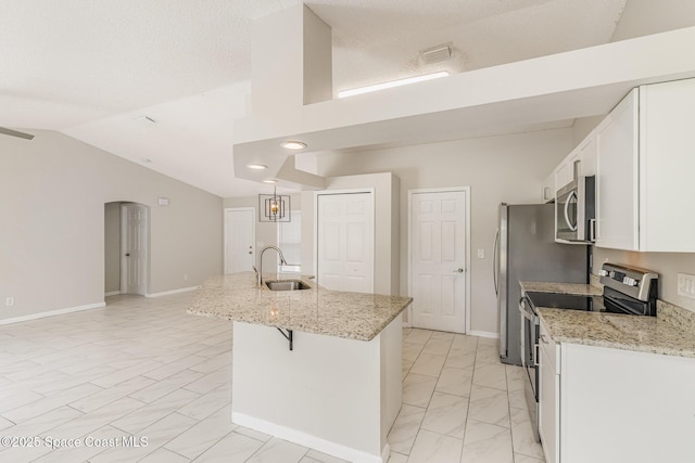 kitchen featuring white cabinets, a kitchen island with sink, a sink, vaulted ceiling, and appliances with stainless steel finishes