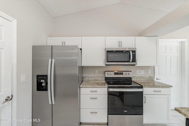 kitchen with vaulted ceiling, white cabinetry, light stone countertops, and stainless steel appliances