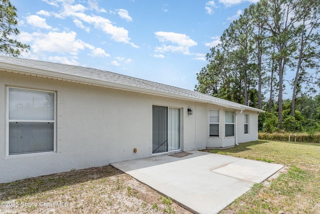 rear view of house featuring a yard, a patio area, roof with shingles, and stucco siding
