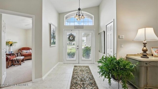 foyer with light tile patterned flooring, a chandelier, baseboards, a high ceiling, and french doors