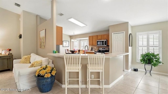 kitchen with light countertops, a kitchen breakfast bar, appliances with stainless steel finishes, a peninsula, and visible vents