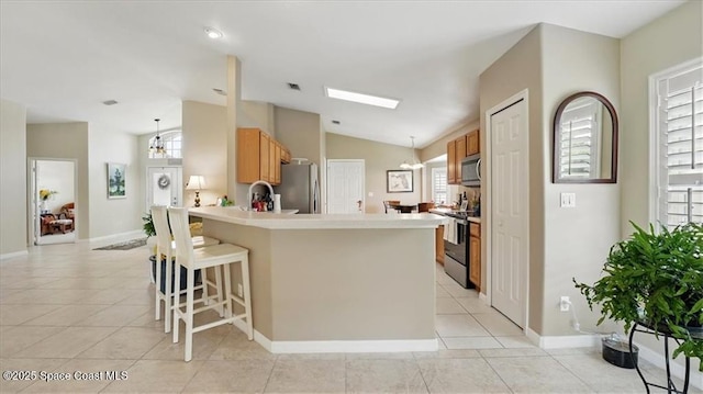 kitchen featuring a peninsula, appliances with stainless steel finishes, a breakfast bar area, vaulted ceiling, and light tile patterned floors