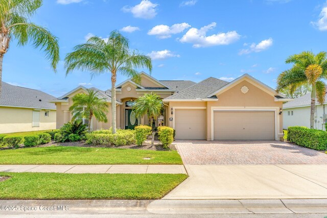 view of front of house featuring a front yard, stucco siding, decorative driveway, and an attached garage