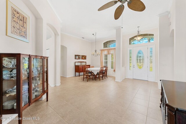 entrance foyer featuring arched walkways, light tile patterned floors, ceiling fan with notable chandelier, baseboards, and crown molding