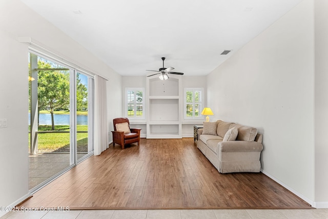sitting room featuring hardwood / wood-style floors, a water view, baseboards, visible vents, and a ceiling fan