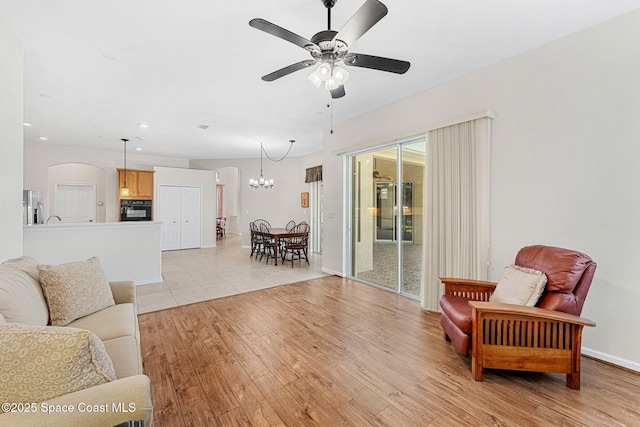 living area with light wood-style flooring, arched walkways, baseboards, recessed lighting, and ceiling fan with notable chandelier