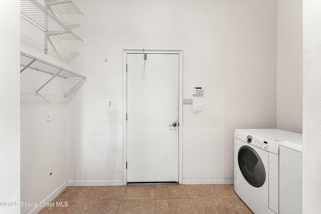 washroom with light tile patterned floors, washer and clothes dryer, laundry area, and baseboards