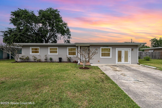 ranch-style home with concrete driveway, french doors, fence, and a front lawn