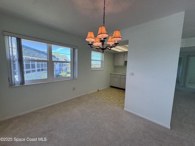 unfurnished dining area with baseboards, a notable chandelier, and light colored carpet