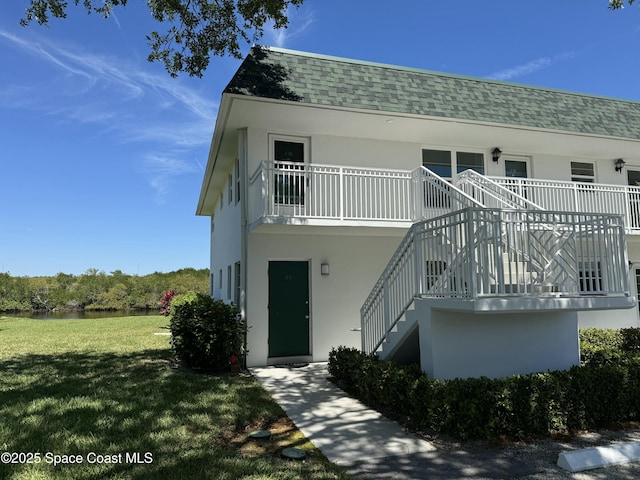 view of front of house featuring stucco siding, a front yard, stairway, and roof with shingles