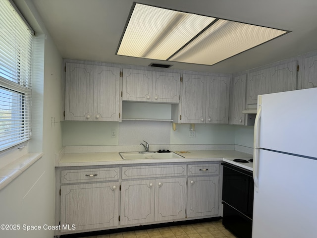kitchen with light countertops, under cabinet range hood, a sink, freestanding refrigerator, and electric range