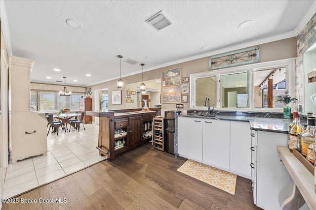 kitchen featuring visible vents, a sink, dark countertops, crown molding, and white cabinetry