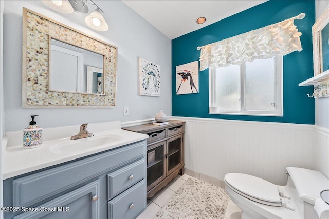 bathroom with tile patterned flooring, vanity, a wainscoted wall, and toilet