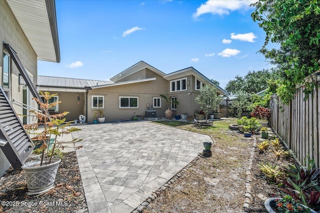 rear view of property featuring a standing seam roof, a fenced backyard, stucco siding, metal roof, and a patio area