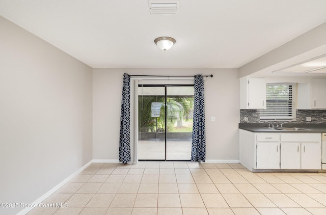 kitchen with white cabinetry, dark countertops, visible vents, decorative backsplash, and a sink