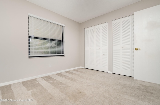 unfurnished bedroom with baseboards, multiple closets, and carpet floors