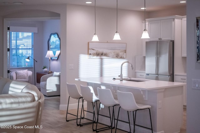 kitchen featuring a sink, a breakfast bar area, freestanding refrigerator, white cabinets, and recessed lighting