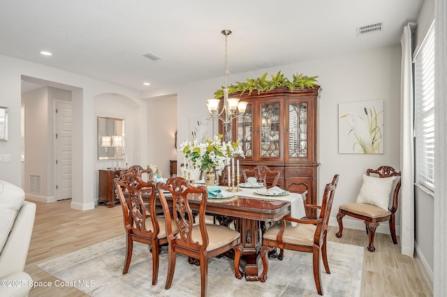 dining area with light wood-type flooring, baseboards, visible vents, and a notable chandelier