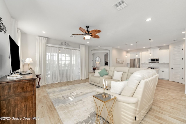 living room featuring a ceiling fan, visible vents, arched walkways, and light wood-style floors