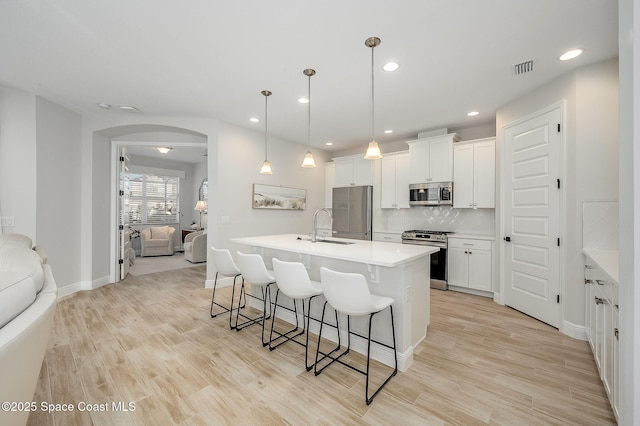 kitchen with stainless steel appliances, a kitchen bar, a sink, and light wood-style floors