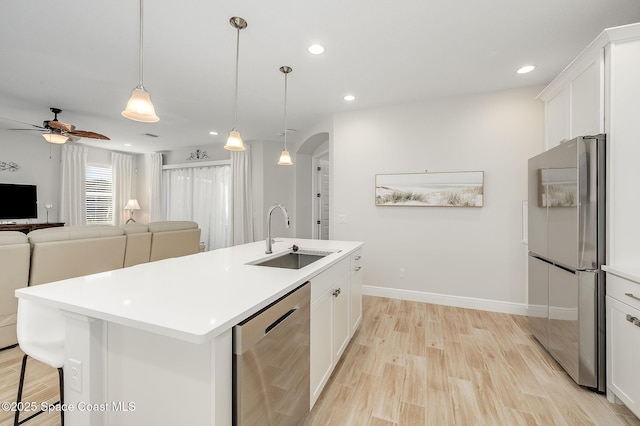 kitchen featuring light wood finished floors, an island with sink, a ceiling fan, a sink, and appliances with stainless steel finishes