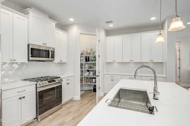 kitchen featuring white cabinets, decorative backsplash, light countertops, decorative light fixtures, and appliances with stainless steel finishes