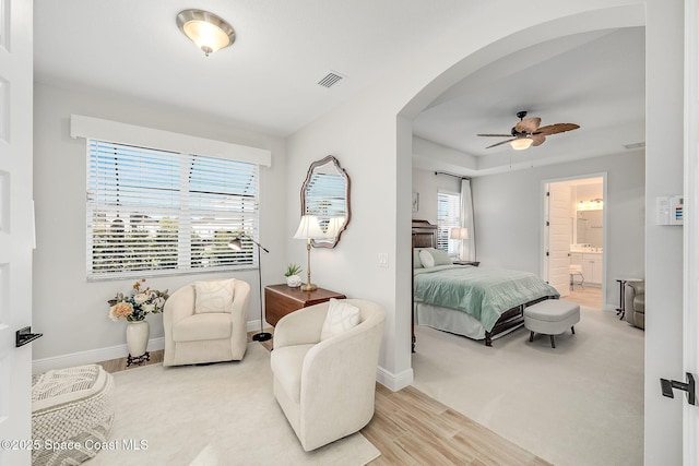 bedroom with arched walkways, ensuite bathroom, visible vents, baseboards, and wood finished floors