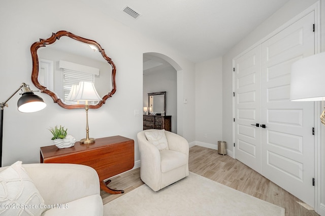 living area with light wood-type flooring, baseboards, visible vents, and arched walkways