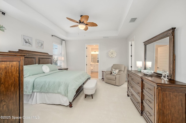bedroom with light carpet, ensuite bathroom, visible vents, and a raised ceiling