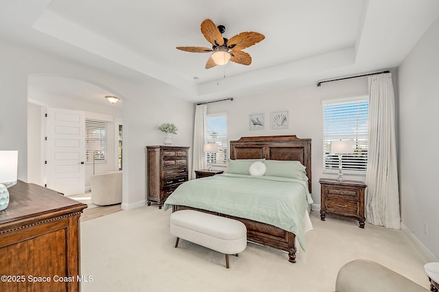bedroom with baseboards, light colored carpet, a raised ceiling, and multiple windows