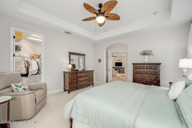 bedroom with arched walkways, a tray ceiling, light colored carpet, baseboards, and visible vents