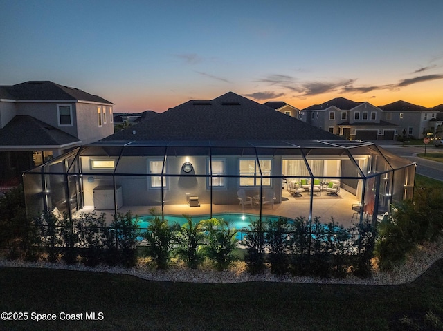 back of property at dusk featuring an outdoor pool, a patio area, glass enclosure, and a shingled roof