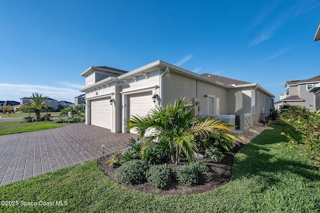 view of side of property featuring a yard, an attached garage, stucco siding, and decorative driveway