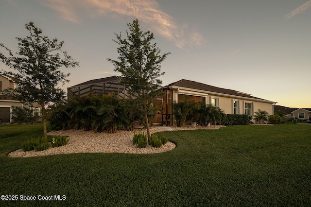 view of front of house with a lawn, a lanai, and stucco siding