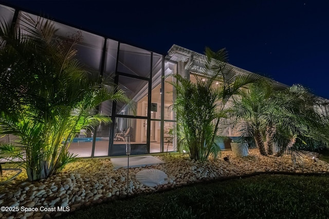 property exterior at night with an outdoor pool, a patio, and glass enclosure