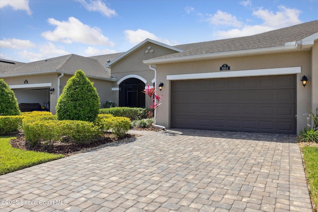 ranch-style home featuring an attached garage, stucco siding, and decorative driveway