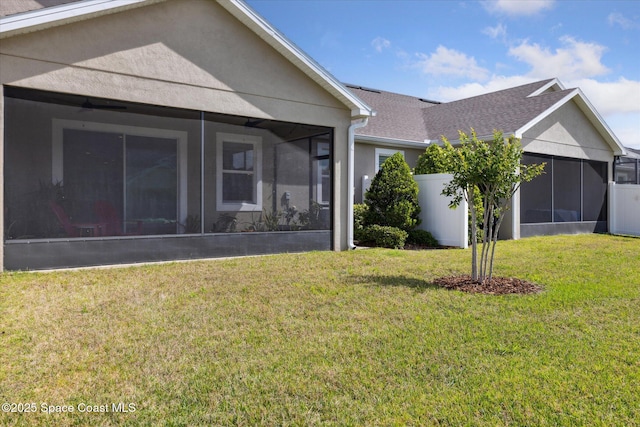 back of house featuring a sunroom, a shingled roof, stucco siding, and a lawn