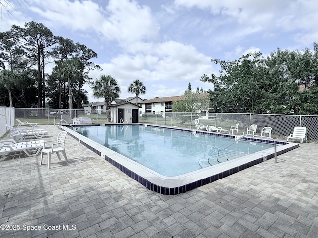 pool with an outdoor structure, a patio area, and fence