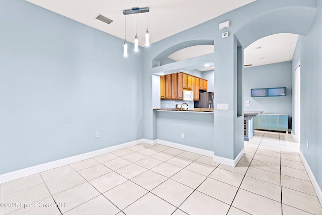 8657 Villanova Dr Unit 901, Cape Canaveral, FL 32920 - kitchen featuring white microwave, brown cabinetry, arched walkways, visible vents, and stainless steel fridge