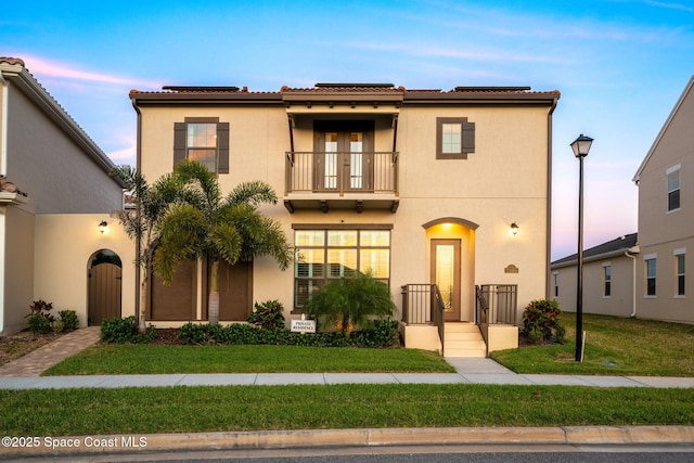 mediterranean / spanish-style house featuring a yard, a balcony, stucco siding, and solar panels