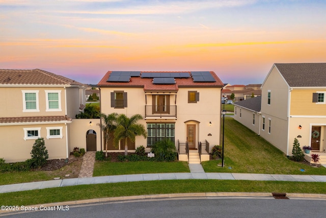 view of front of home featuring roof mounted solar panels, a tiled roof, a lawn, stucco siding, and a balcony