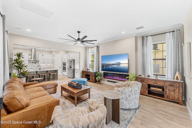 living room with crown molding, a ceiling fan, visible vents, and light wood-type flooring