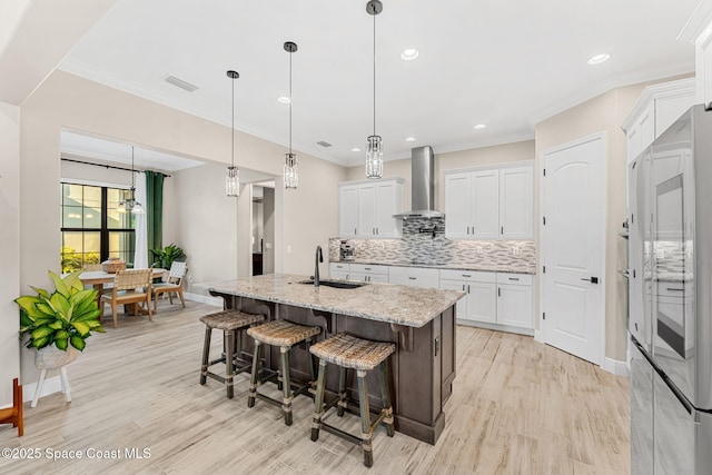 kitchen featuring tasteful backsplash, white cabinets, visible vents, wall chimney exhaust hood, and a sink