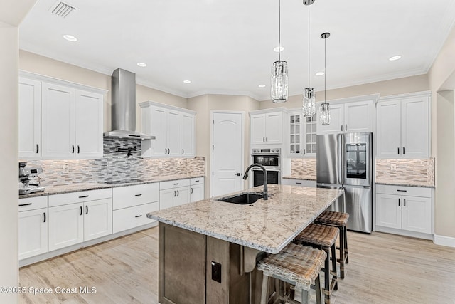 kitchen with wall chimney exhaust hood, white cabinetry, visible vents, a sink, and stainless steel appliances