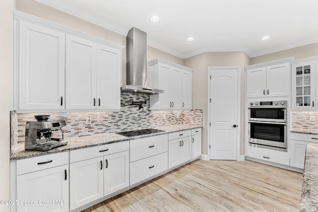 kitchen with crown molding, light wood-style floors, wall chimney exhaust hood, white cabinets, and black electric stovetop