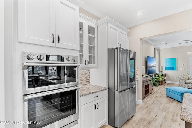 kitchen featuring glass insert cabinets, ornamental molding, open floor plan, appliances with stainless steel finishes, and white cabinetry