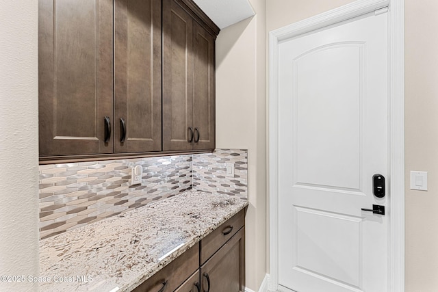interior space with tasteful backsplash, light stone countertops, and dark brown cabinetry